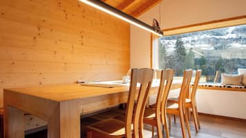 Ein Holzinterieur mit Esstisch, Stühlen, einem Fenster mit Aussicht und einer Pendelleuchte.