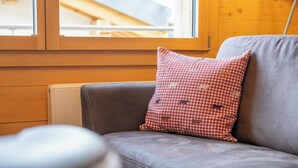 A grey leather sofa with a red and white checkered pillow, a wooden radiator, and a window with a view of a building.