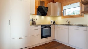 A modern kitchen with white cabinets, a black oven, and a window with a view of trees.