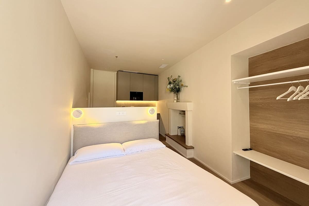 Un dormitorio moderno con cama, mesitas de noche, espejo, armario y pared de paneles de madera.