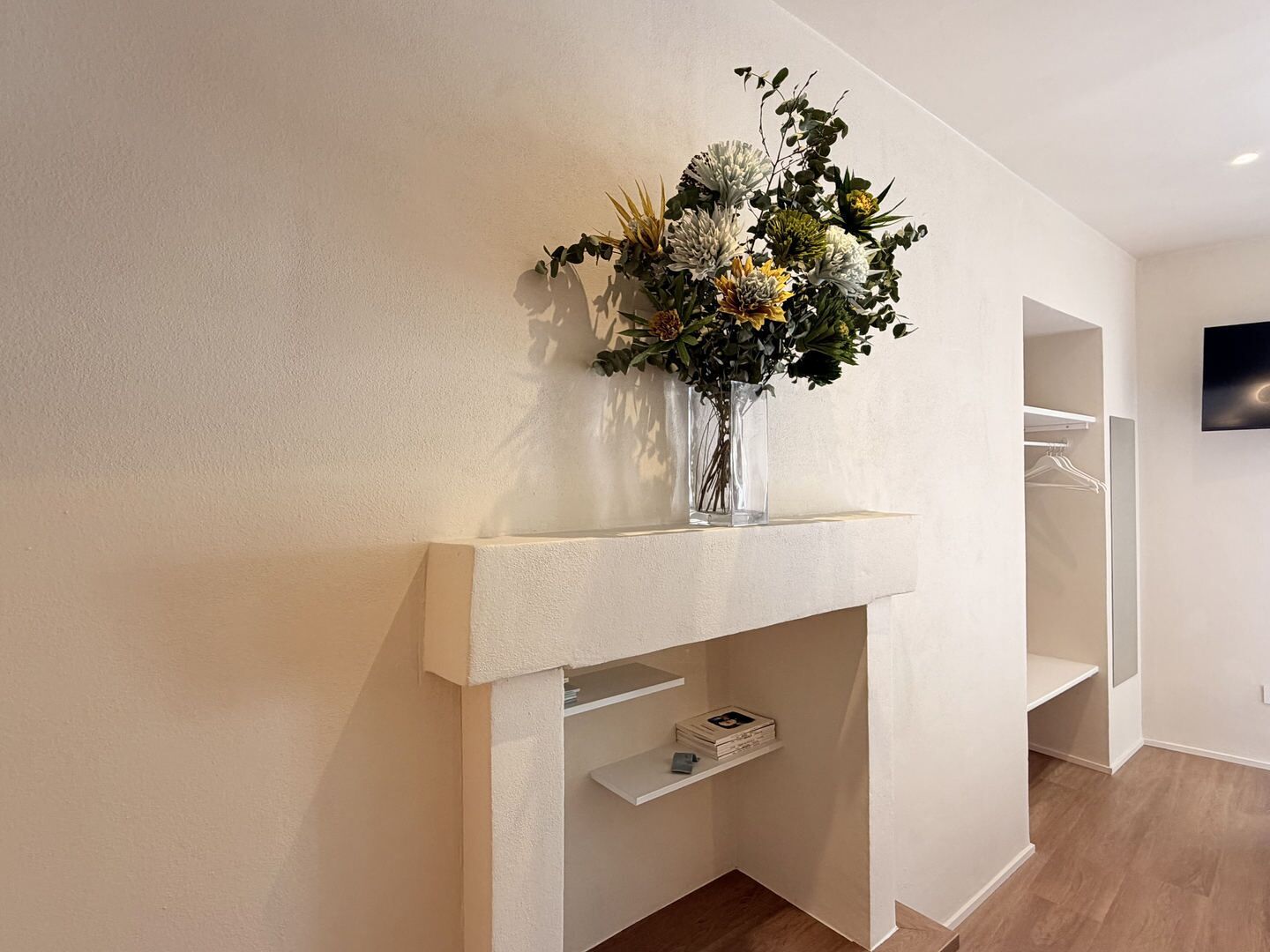 Una habitación moderna con una chimenea blanca, un televisor montado y piso de madera.