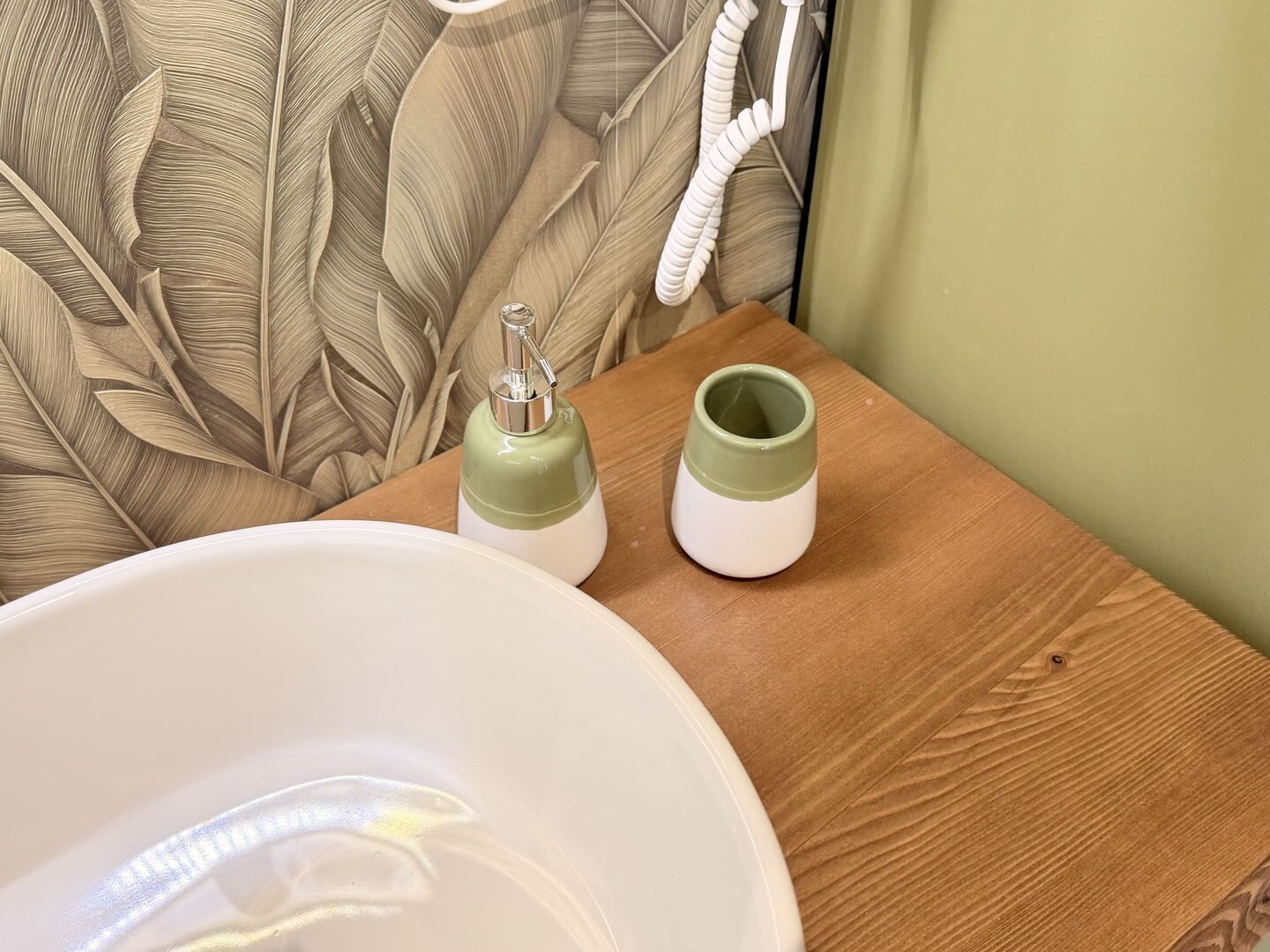 A bathroom with a white sink, a green and white soap dispenser, and a green and white cup on a wooden surface.