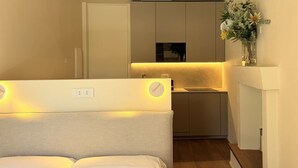 Un dormitorio con cama, mesita de noche y una pequeña zona de kitchenette con fregadero y encimera.