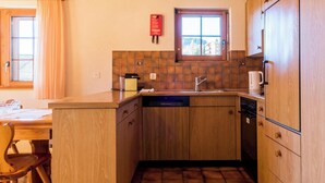 Cocina compacta con muebles de madera, lavavajillas integrado y ventana con vistas.