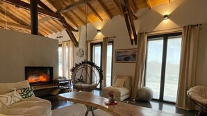 Ein gemütliches Wohnzimmer mit Kamin, bequemen Sitzgelegenheiten und großen Fenstern.