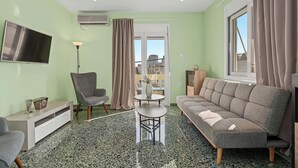 Un salon comprenant un canapé, un fauteuil, un téléviseur et une petite table sur laquelle est posé un vase.