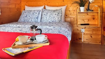 A wooden cabin bedroom with a bed, bedside table, and a wall-mounted picture.