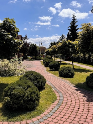 Un sendero pavimentado serpentea por una zona ajardinada con arbustos y árboles podados.