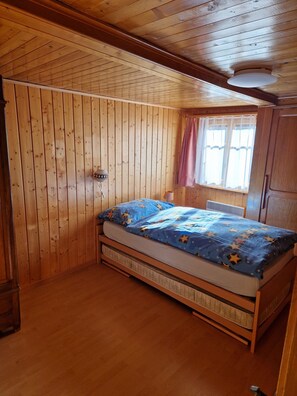 Camera da letto in una casetta di legno, con un letto, una finestra con tende e una lampada a parete.