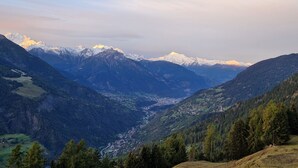 Eine gebirgige Landschaft mit schneebedeckten Gipfeln, einem Tal mit einer kleinen Siedlung und dichten bewaldeten Gebieten.