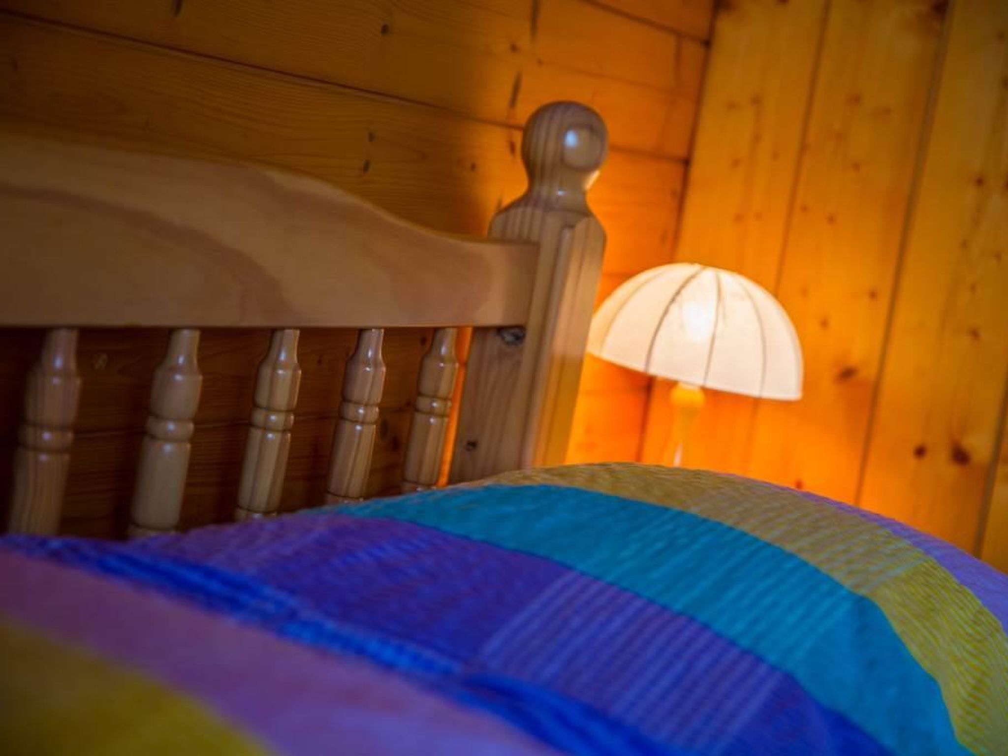 Cabecera de madera con una lámpara junto a una cama con colcha colorida.