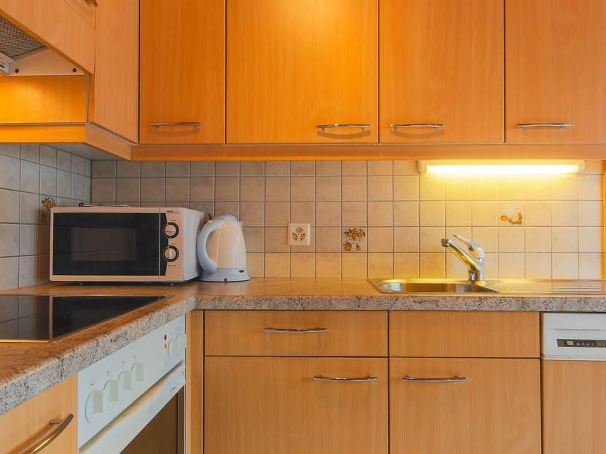 A kitchen with wooden cabinets, a microwave, a kettle, a sink, and a dishwasher.