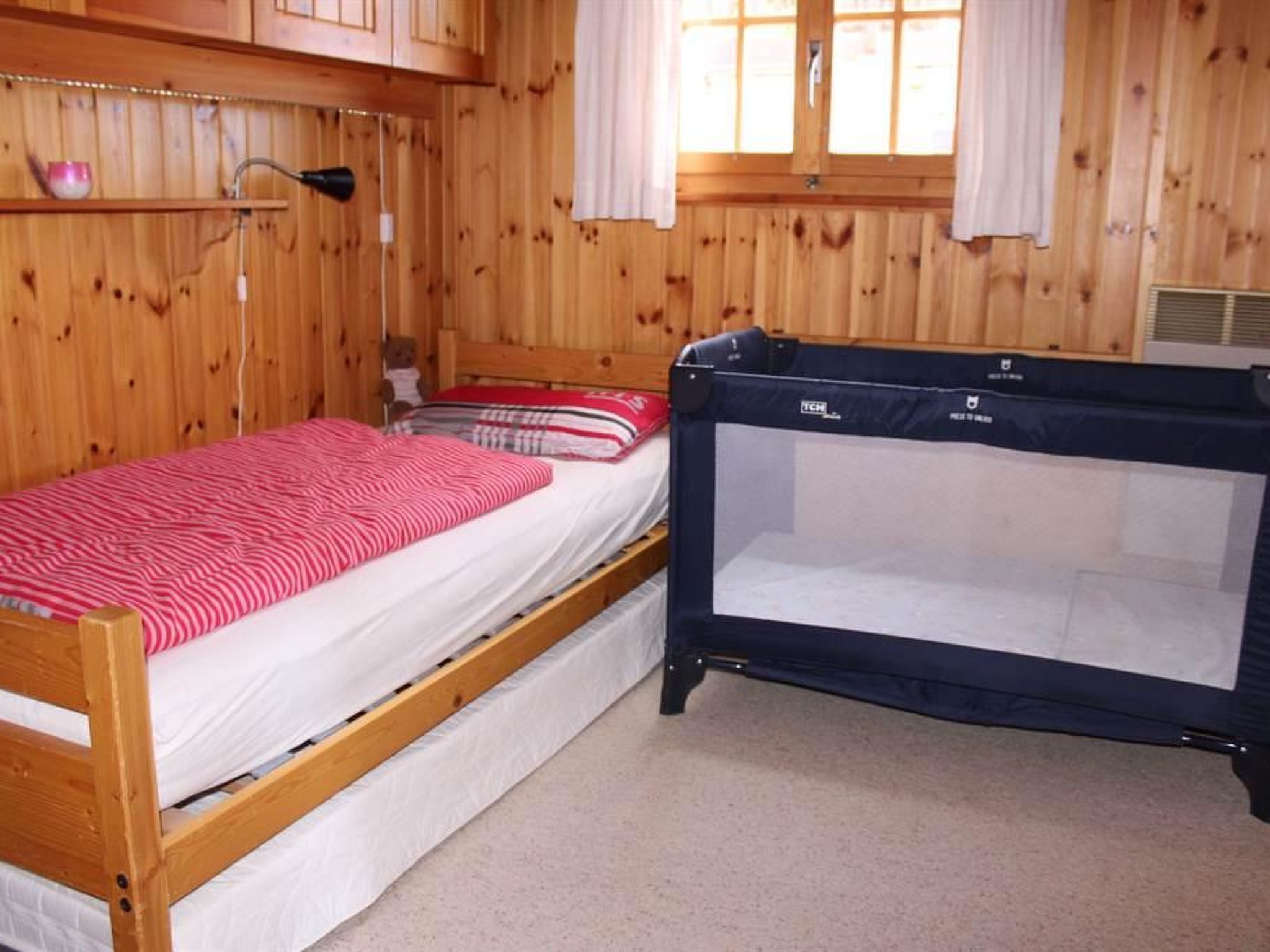 Quarto com uma cama beliche de madeira, um berço, uma janela com cortinas e uma prateleira com uma xícara.