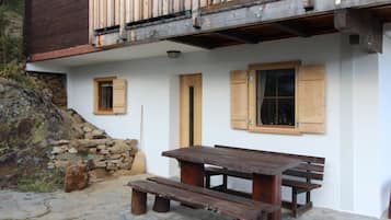 A rustic wooden building with a stone staircase, a wooden deck, and a picnic table with benches.