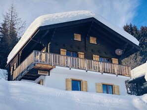Un chalet en bois doté d’un balcon, de nombreuses fenêtres et d’un toit recouvert de neige.