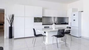 Une cuisine moderne avec des meubles blancs, un îlot central, des chaises noires et un réfrigérateur blanc.