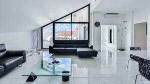 Un salon moderne avec une table basse en verre, un canapé en cuir noir et une grande fenêtre donnant sur la ville.