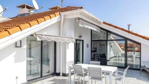 Une terrasse moderne sur le toit, dotée d’un espace repas, de portes vitrées et d’un toit recouvert de tuiles.