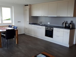 A modern kitchen with white cabinets, a black stove, and a dining area with a table and chairs.