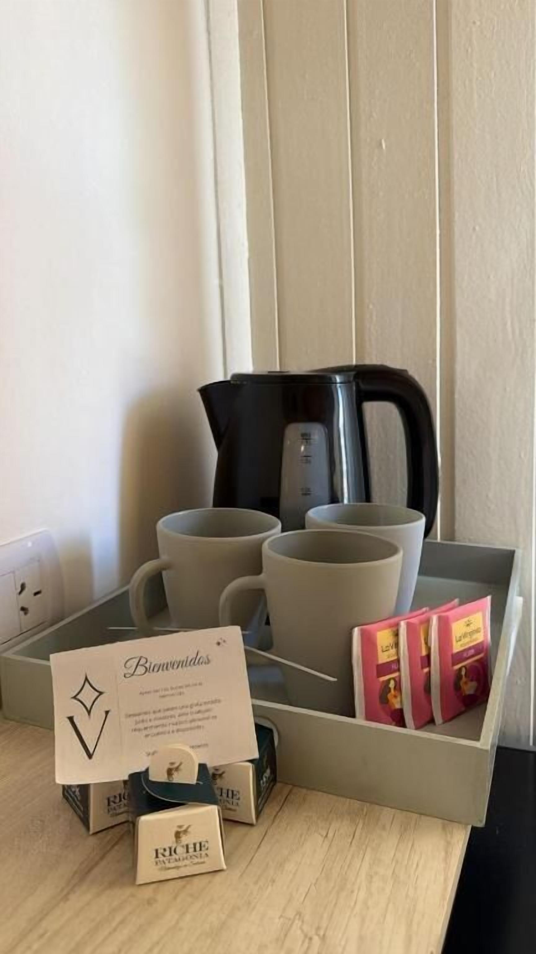 A tray with a black kettle, two grey mugs, a card labeled 'Bemvidos,' and two boxes of 'Roche' products.