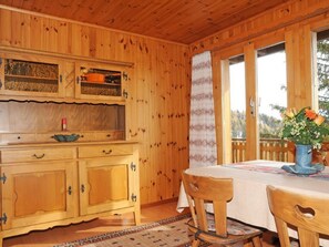 A wooden interior with a dining table, chairs, a cabinet, and a window with a view.