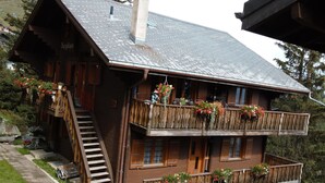 Un chalet en bois à deux étages, doté d’un balcon, d’un escalier et de jardinières.