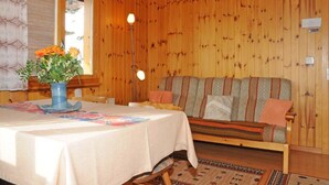 L’intérieur d’un chalet en bois, avec une table à manger, un canapé et une fenêtre avec des rideaux.