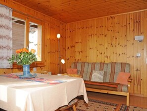 A wooden cabin interior with a dining table, a sofa, and a window with curtains.