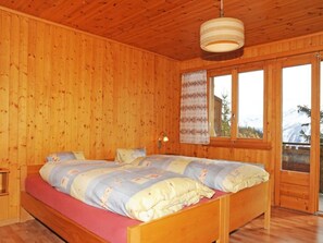 A wooden-paneled bedroom with a bed, a nightstand, a lamp, and a window with a view of the outdoors.