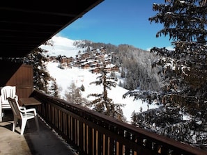 Balcón de madera con vista a una zona montañosa cubierta de nieve y edificios.