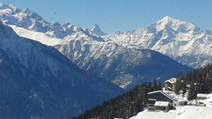 Un paysage de montagne avec des sommets enneigés et un bâtiment doté d’un toit en pente.