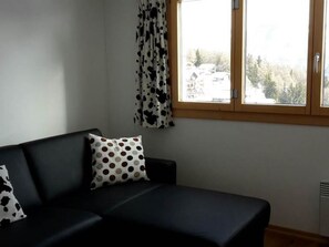 A room with a black sofa, a window with a view of trees, and a curtain with a cow pattern.