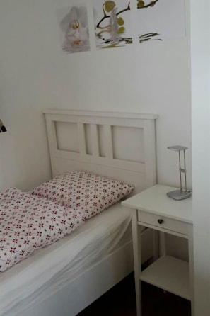 Un dormitori amb un llit, una taula de nit i una làmpada penjada a la paret.