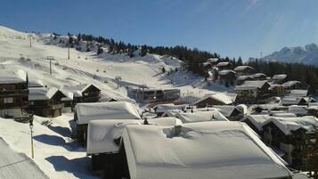 Un poble cobert de neu amb edificis de fusta, un teleàs i muntanyes al fons.