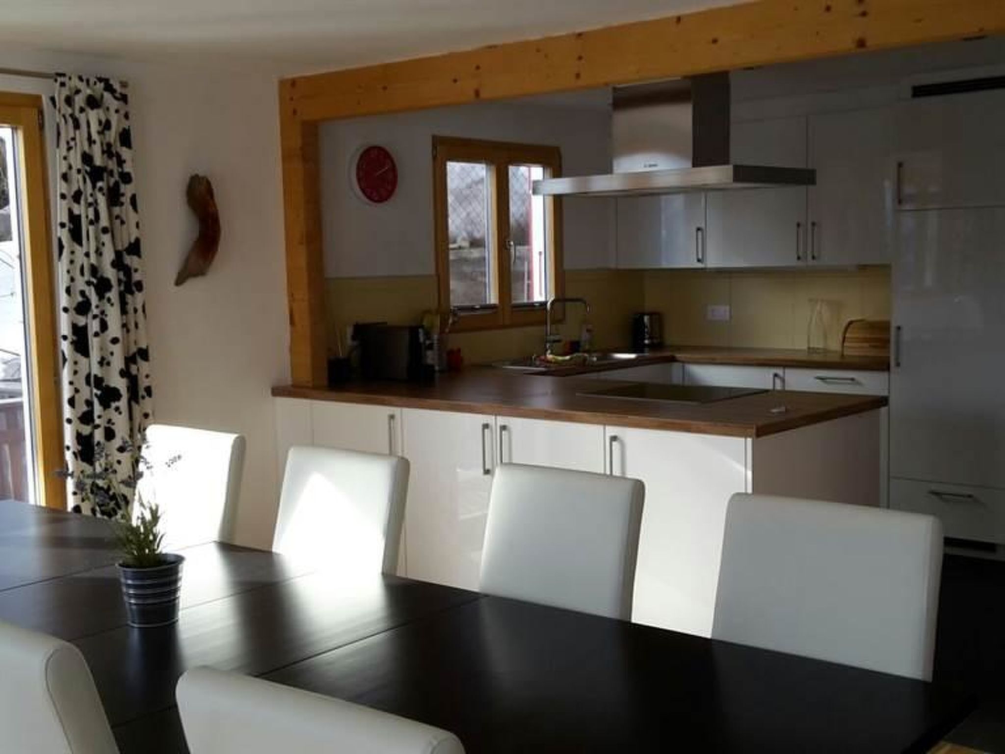 Zona pranzo con tavolo e sedie, cucina con pensili e lavello, e finestra con tende.