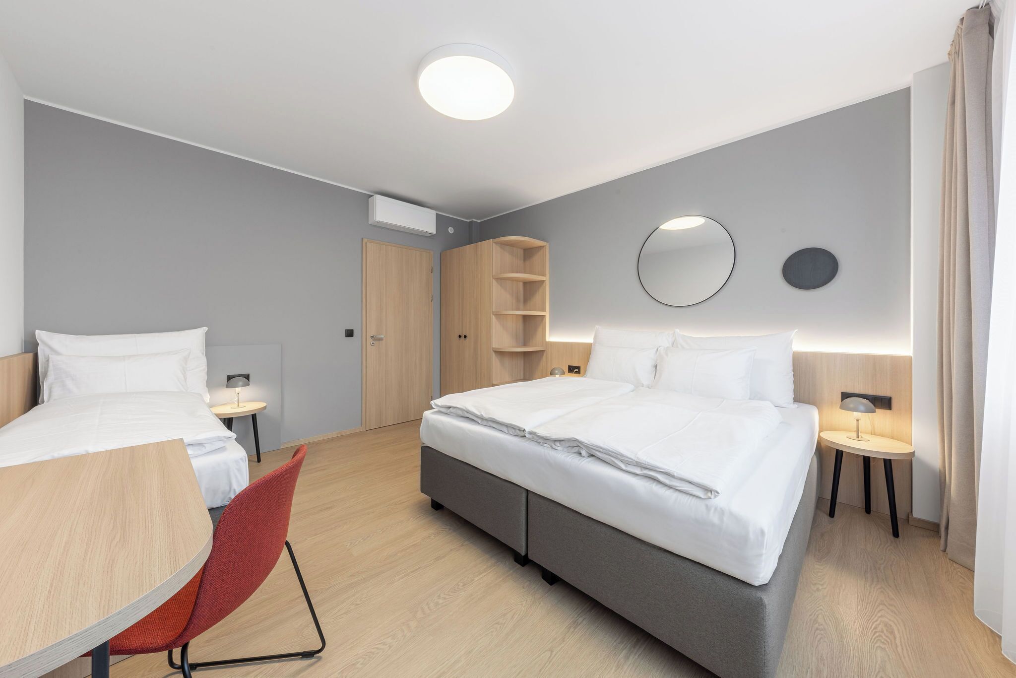 Una habitación de hotel con cama, escritorio, silla, armario y espejo.