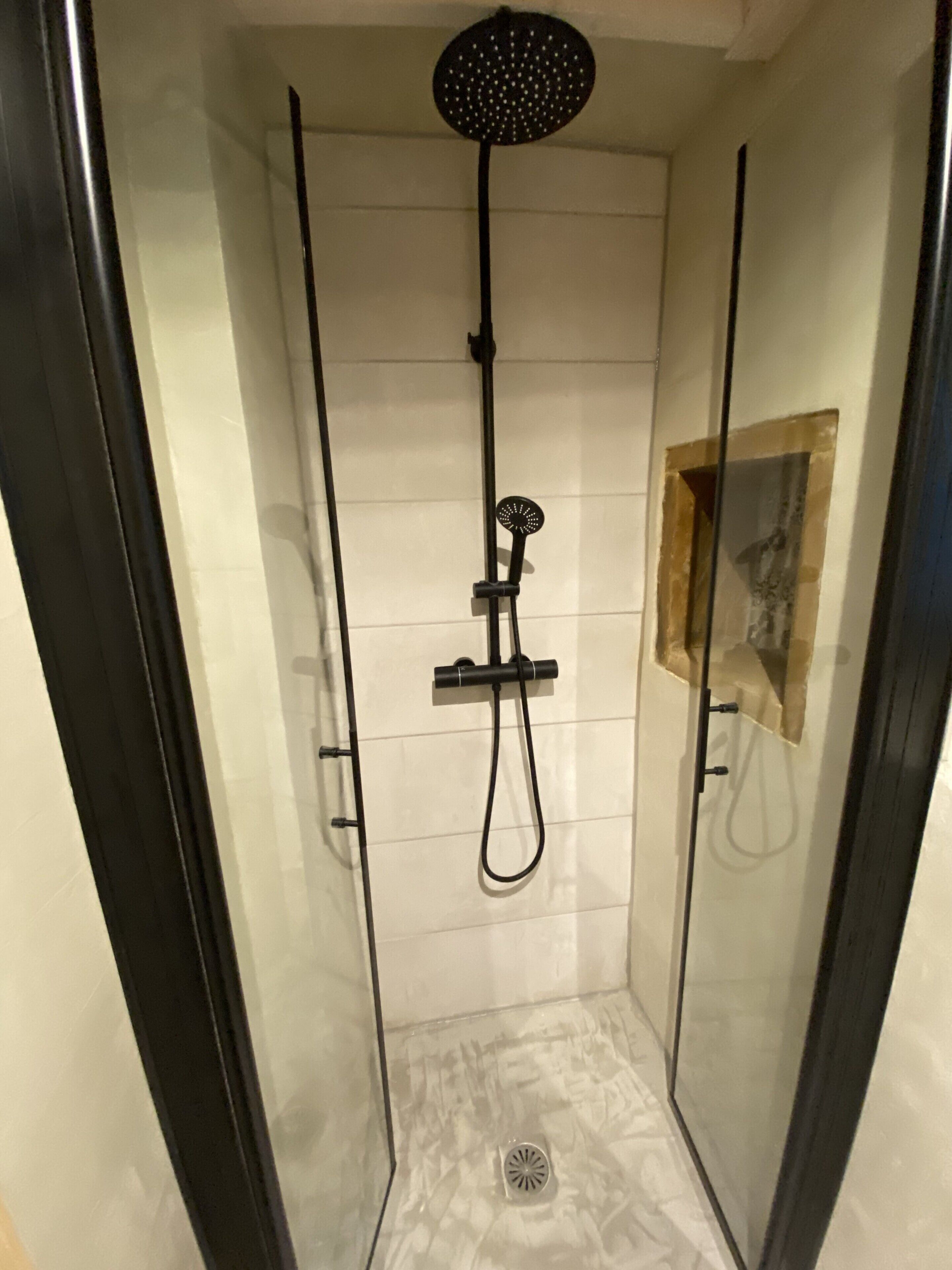 En duschkabin med glasväggar, en duschslang med justerbart duschhuvud och en väggmonterad blandare.