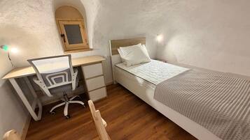 Une chambre avec un bureau en bois, un lit, une chaise et une petite fenêtre en arc de cercle.