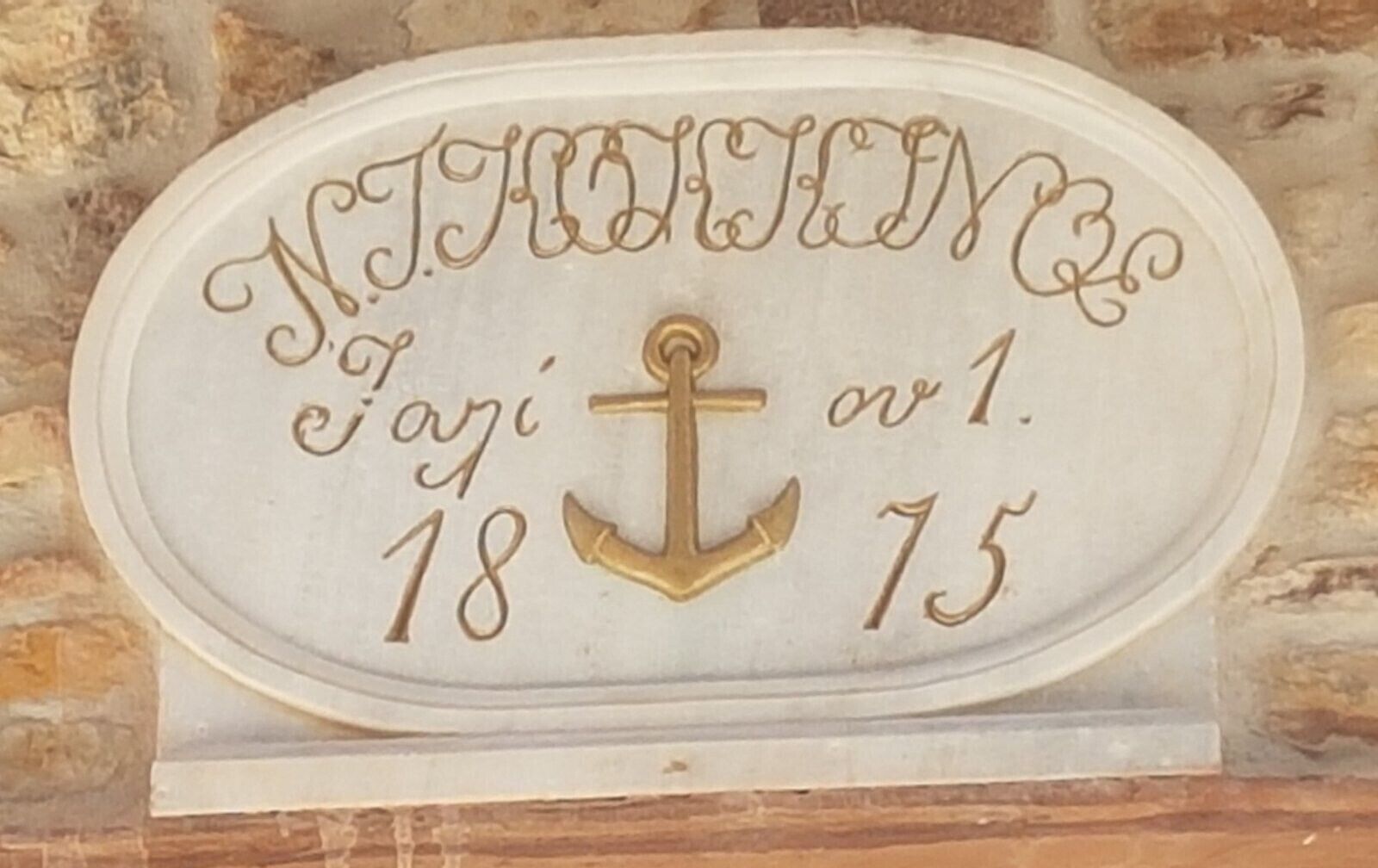 A white plaque with gold lettering and an anchor symbol, displaying the text 'N. J. FRENCH 18 75'.