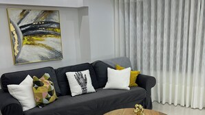 Una sala de estar moderna con un sofá negro, una mesa de centro de madera y un cuadro abstracto grande en la pared.