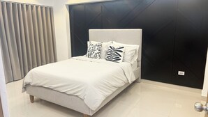 Un dormitorio moderno con una cama, cabecera oscura y ventana con cortinas.