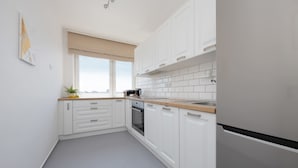 Une cuisine moderne avec des meubles blancs, un réfrigérateur en acier inoxydable et une fenêtre offrant une belle vue.
