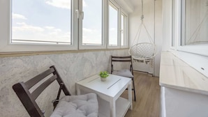 Une pièce avec une table blanche, deux chaises, un fauteuil suspendu et une vue sur le ciel par de grandes fenêtres.