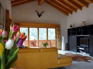 A living room with a yellow sofa, a fireplace, a TV, and a large window with a view of trees. - LuxLax 2. OG Süd Appartement/Fewo, Dusche oder Bad, WC by Interhome (Lax)