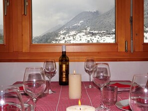 A dining table with wine glasses, a candle, and a bottle of wine, set against a backdrop of a snowy mountain view through a window. - LuxLax 2. OG Süd Appartement/Fewo, Dusche oder Bad, WC by Interhome (Lax)
