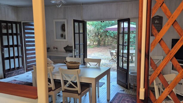 A room with a dining table, chairs, a basket, a television, and a view of the outdoors. - Lège-Cap-Ferret, a wooden house just 5 minutes from the bay and the ocean (Lège-Cap-Ferret)
