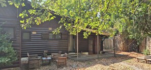 Une cabane rustique en rondins de bois, dotée d’une véranda, de bancs en bois et d’une pergola recouverte de feuillage verdoyant.
