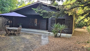 A rustic log cabin with a covered patio, a small table and chairs, and a potted plant. - Lège-Cap-Ferret, a wooden house just 5 minutes from the bay and the ocean (Lège-Cap-Ferret)