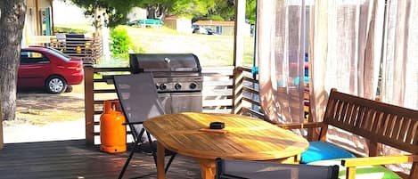 Ein überdachter Außenbereich mit Grill, Stühlen und Tisch.