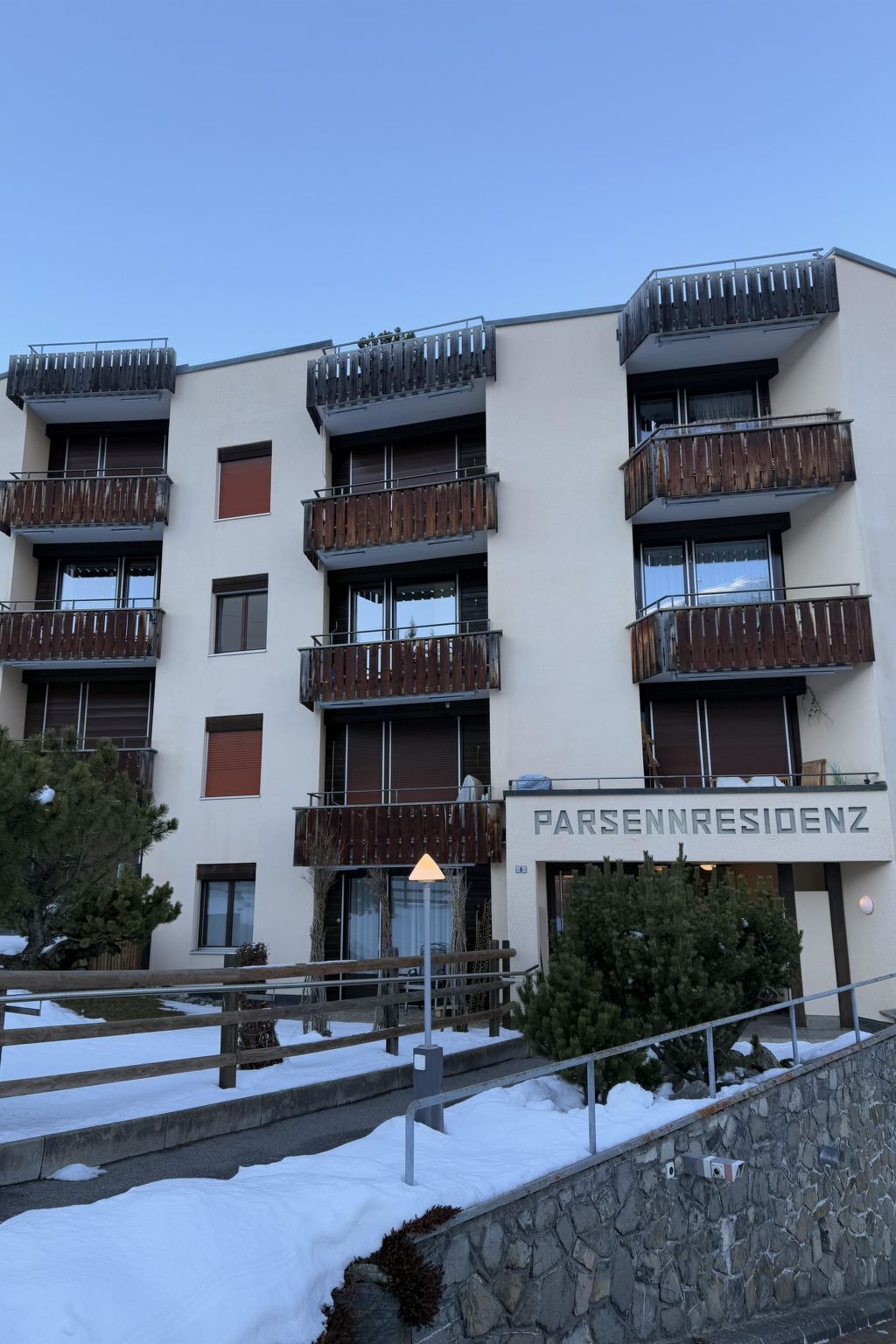 A multi-story building with balconies, a stone wall, and a sign reading 'PARSENNRESIDENZ'.